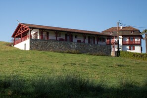 Edifici de dues plantes amb façana de pedra, detalls vermells i un balcó al pis superior.