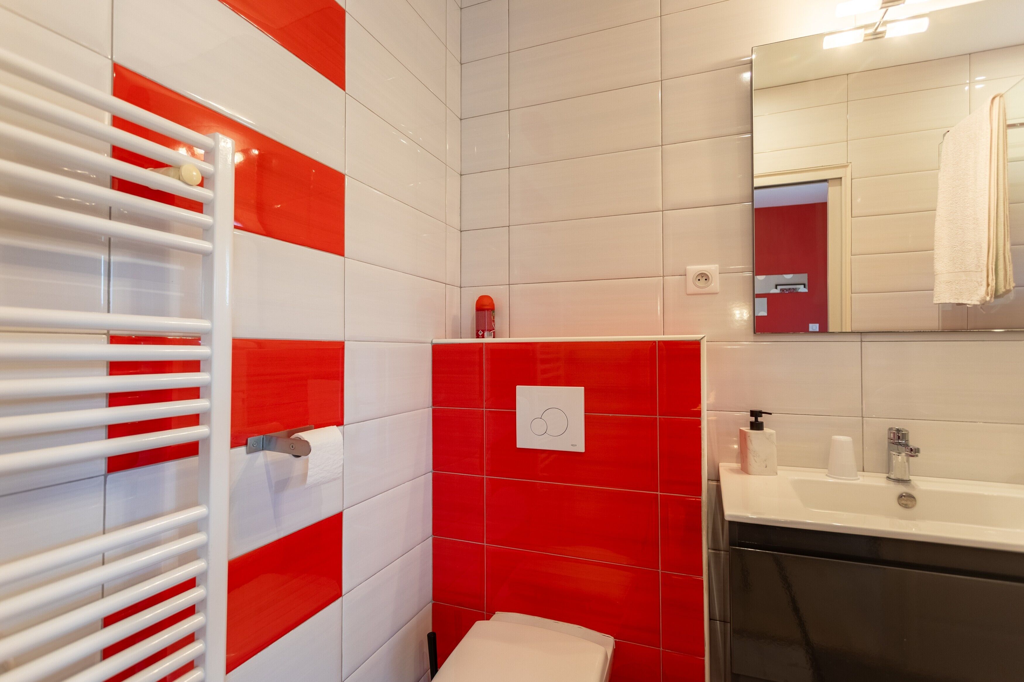 A bathroom with red and white tiles, a white sink, a mirror, and a towel rack.