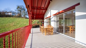 Un espacio al aire libre cubierto con una mesa y sillas, una baranda roja y una vista de una casa al fondo.