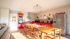 Una cocina moderna con armarios rojos, un refrigerador de acero inoxidable y una zona de comedor con sillas de madera y una mesa.