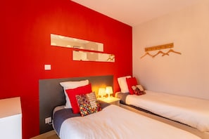 Une chambre d’hôtel avec deux lits, des murs rouges, un miroir et un porte-manteau.