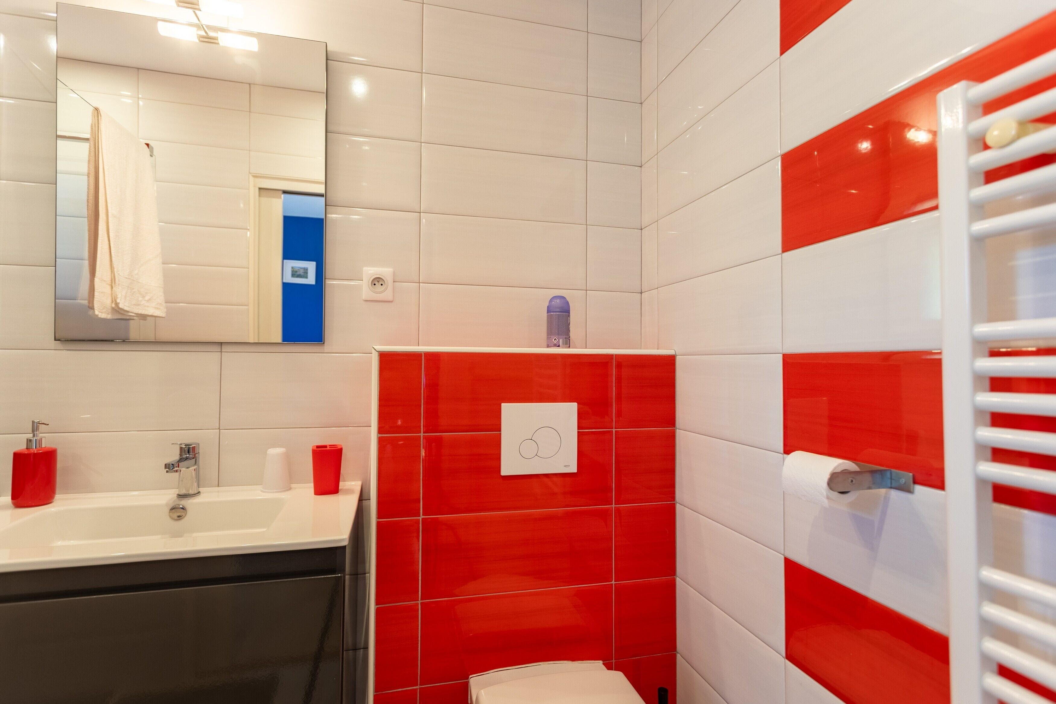 A bathroom with a white sink, red and white tiles, a mirror, and a towel rack.