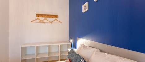Une chambre à coucher avec un lit, une console blanche, un mur bleu et un luminaire fixé au mur.
