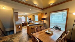A spacious kitchen with wooden cabinets, a central island, and a dining area with a wooden table and chairs. - Prime Base Location! 5BR, 4BA condo just a 2-min walk to the Express Quad. Ski back to your door. Features 2 hot tubs and a double garage for gear. Enjoy easy access to base restaurants and bars! (Kimberley)