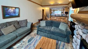 A living room with a grey sofa, a patterned rug, and a fireplace with stone accents. - Prime Base Location! 5BR, 4BA condo just a 2-min walk to the Express Quad. Ski back to your door. Features 2 hot tubs and a double garage for gear. Enjoy easy access to base restaurants and bars! (Kimberley)