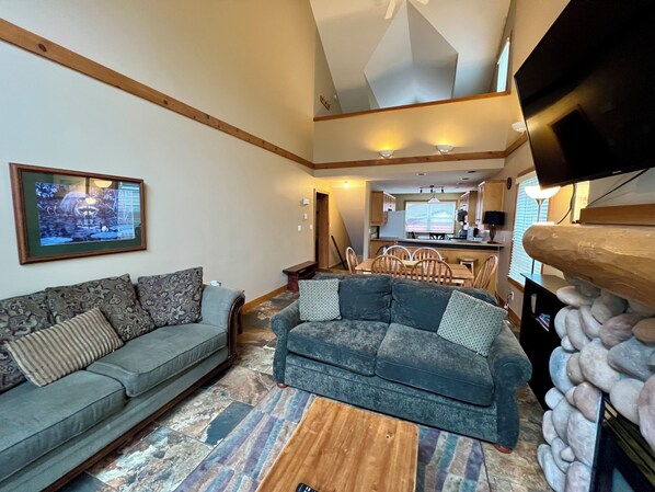 A living room with a grey sofa, a patterned rug, and a fireplace with stone accents.