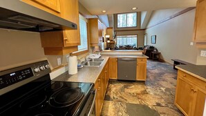 A modern kitchen with wooden cabinets, a black stove, a dishwasher, and a stone-tiled floor. - Prime Base Location! 5BR, 4BA condo just a 2-min walk to the Express Quad. Ski back to your door. Features 2 hot tubs and a double garage for gear. Enjoy easy access to base restaurants and bars! (Kimberley)