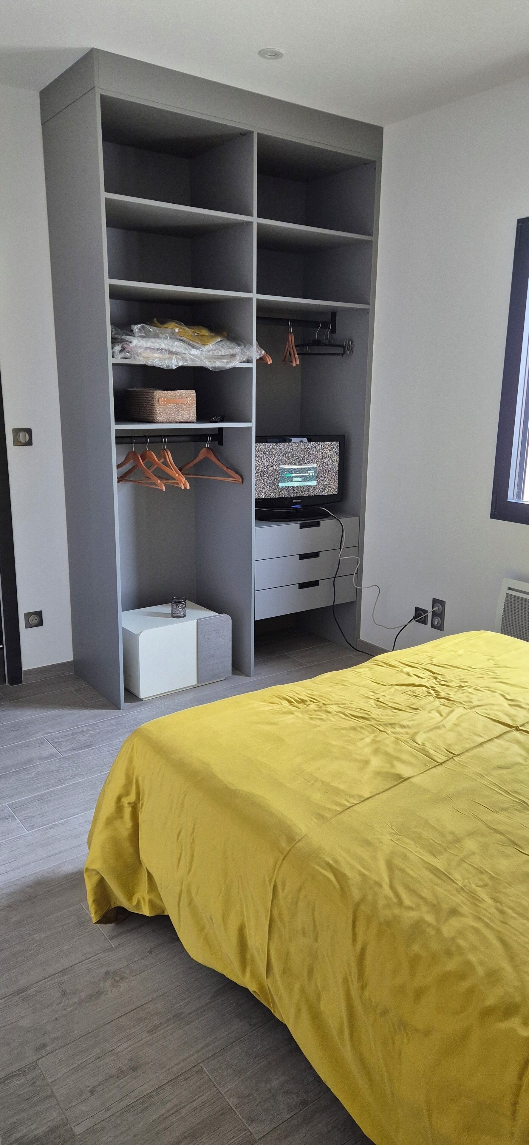 A bedroom with a large wardrobe, a bed with a yellow bedspread, and a television on a stand.