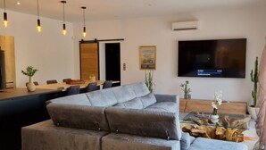 A modern living room with a grey sectional sofa, a glass coffee table, and a flat-screen TV mounted on the wall. - Contemporary house at the gateway to the Luberon in a peaceful and relaxing setting (Pernes-les-Fontaines)