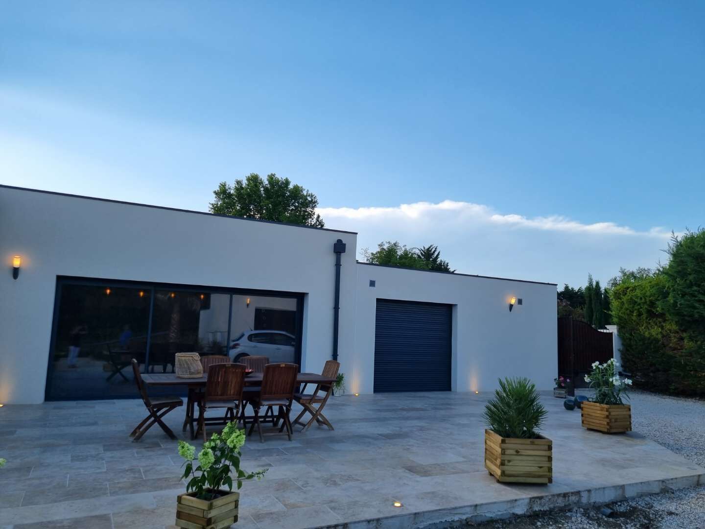 Ein modernes Haus mit Terrasse, Essbereich mit Holzmöbeln und Garage.