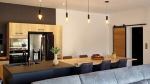 A modern living room with a grey sofa, a wooden dining table, and pendant lighting. - Contemporary house at the gateway to the Luberon in a peaceful and relaxing setting (Pernes-les-Fontaines)