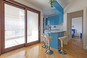 A modern kitchen with a central island, bar stools, and a sliding glass door leading to an outdoor area. - Appartamento Torretta 4 -Immobili e Soluzioni Rent (Bergamo)