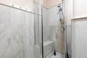 A glass-enclosed shower with a marble floor and a white shelf. - Bed&Art - Immobili e Soluzioni Rent (Bergamo)