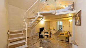 Ein geräumiger Innenraum mit Wendeltreppe, Essbereich und Wohnbereich inklusive Sofa und Fernseher.