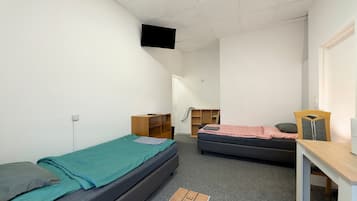 A dormitory room with two single beds, a desk, a chair, a TV mounted on the ceiling, and a wardrobe.