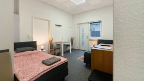 Een slaapkamer met een bed, bureau, stoel en een klein raam.