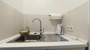 Een kleine keuken met een spoelbak, een kraan, een zeepdispenser, een rek voor keukenpapier en een stopcontact.