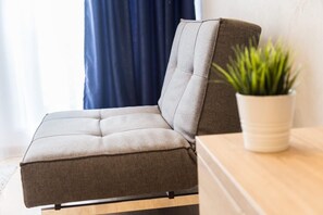 A modern sofa with a cushioned backrest and armrests, positioned on a wooden floor against a wall with a potted plant. - Back suites (Belgrade)