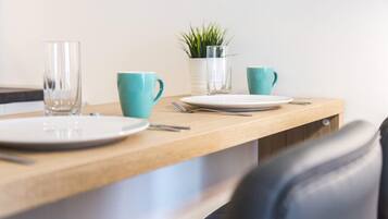 A dining area with a wooden table, two plates, two cups, a fork, a knife, and a small potted plant.