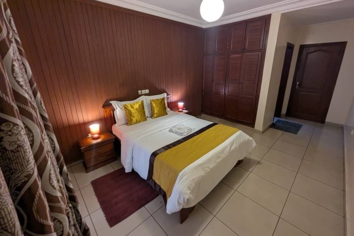 A bedroom with a bed, wooden panel walls, a nightstand, and a door.