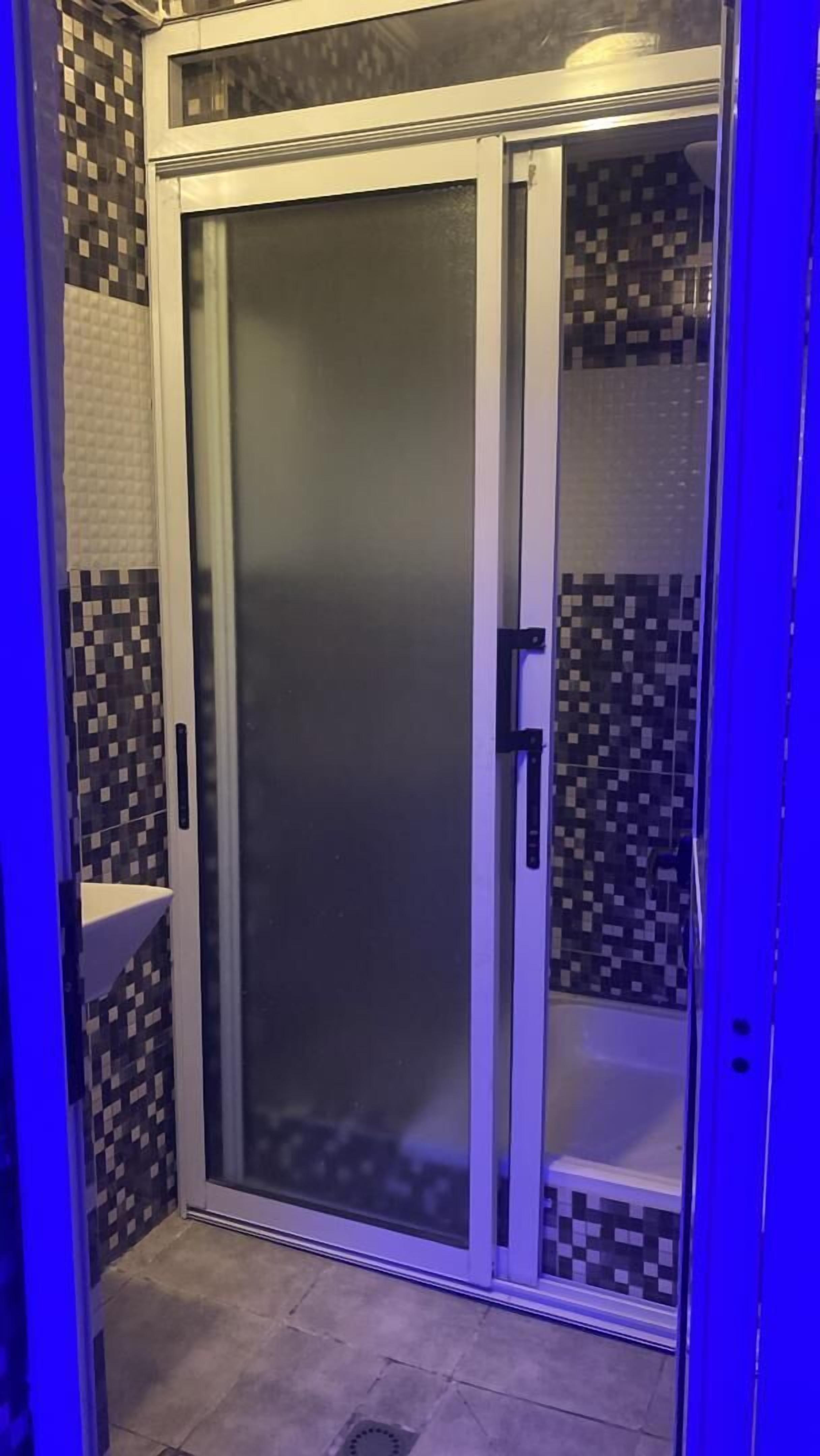 Een badkamer met een glazen deur, betegelde wanden en een douchehoek.