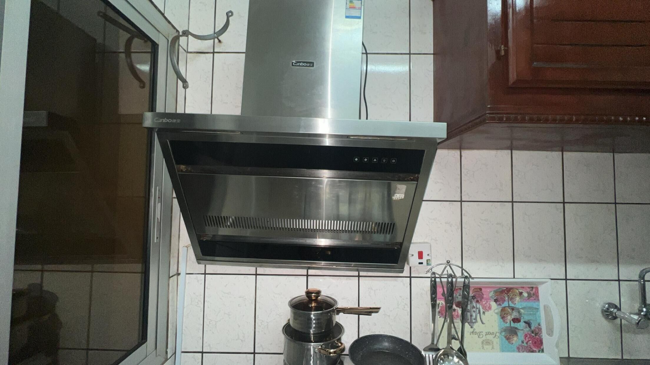 A kitchen with a stainless steel range hood, white tiled backsplash, and a coffee maker on the counter.