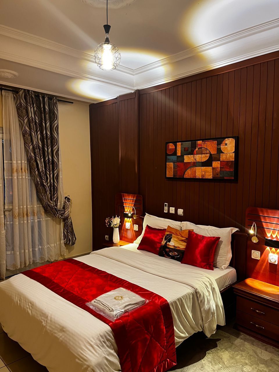 A hotel room with a large bed, wooden paneling on the walls, a ceiling light fixture, and a wall-mounted artwork.