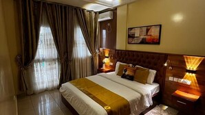Una camera d'albergo con un letto grande, una testiera in legno, un comodino con una lampada, una finestra con tende e un lampadario.