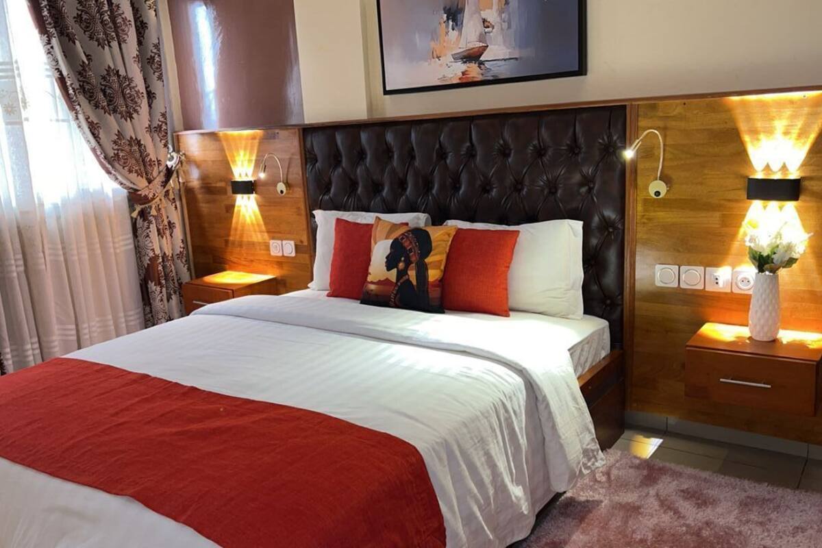 A neatly made bed with a red and white bedspread, two bedside lamps, a nightstand with a vase, and a framed picture above the bed.