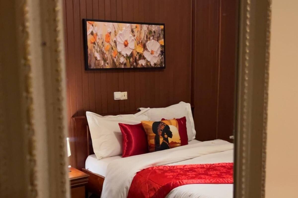 A bedroom with a bed, pillows, a nightstand, a wall-mounted painting, and a carpeted floor.