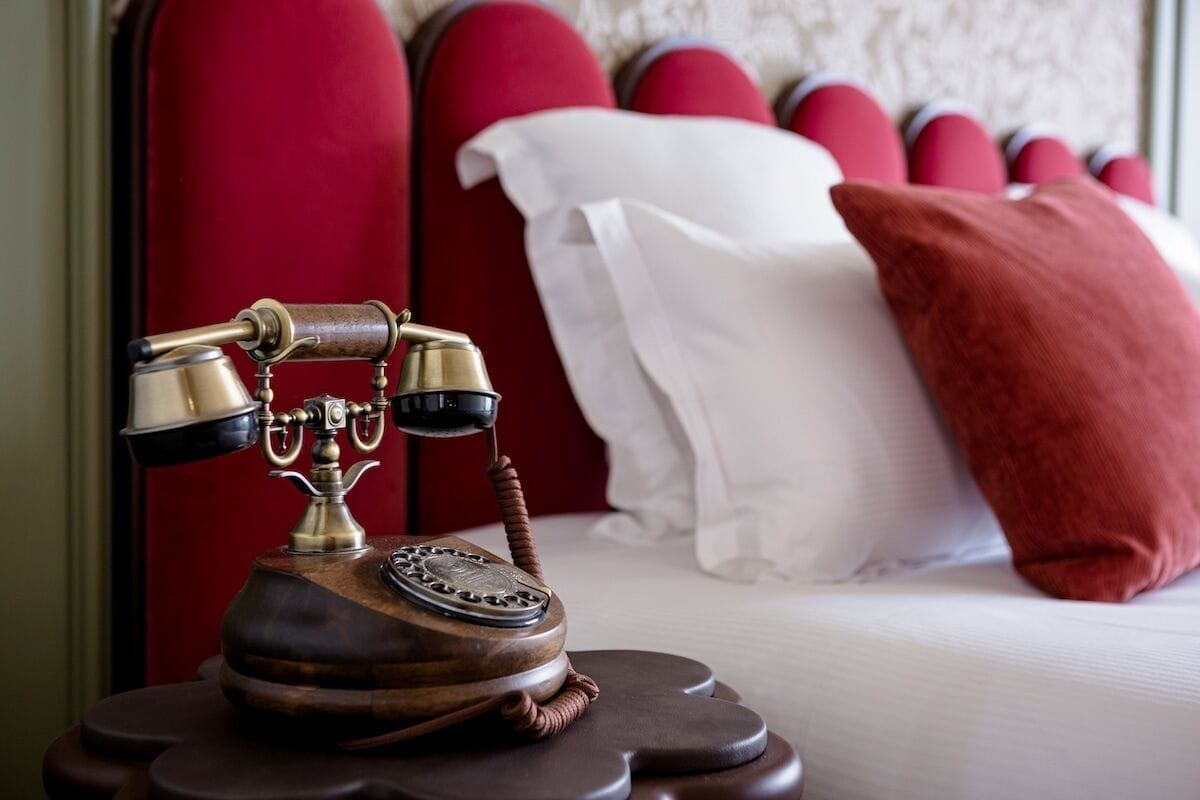 A vintage rotary phone on a bedside table in a room with a red upholstered headboard and white bedding.