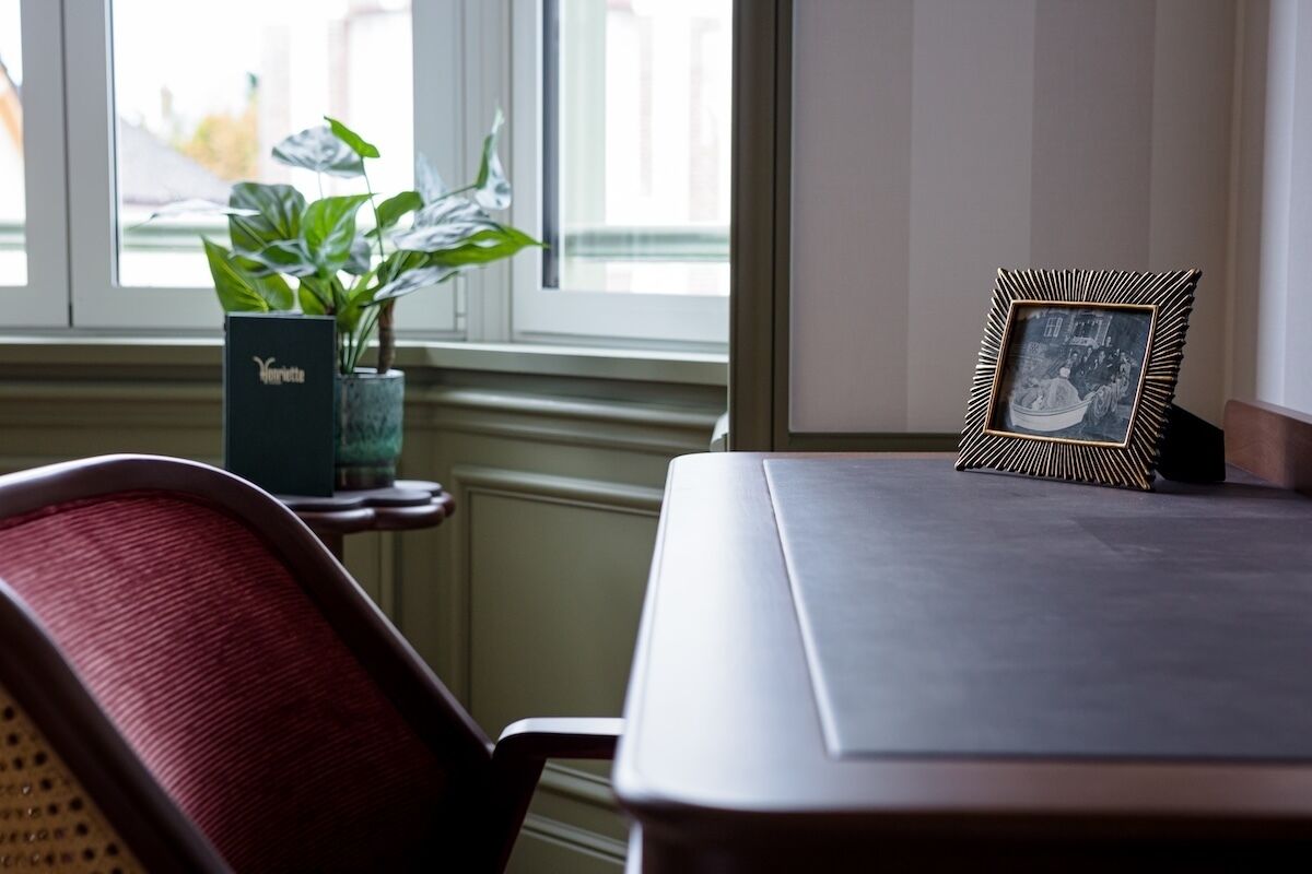 Una habitación con ventana, una planta en un florero, una fotografía enmarco y una silla.