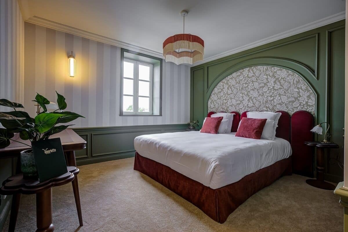 A bedroom with a large bed, a desk, a chair, a potted plant, and a window.