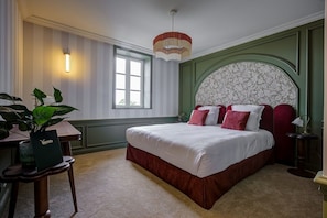 A bedroom with a large bed, a desk, a chair, a potted plant, and a window. - VILLA HENRIETTE (Cabourg)