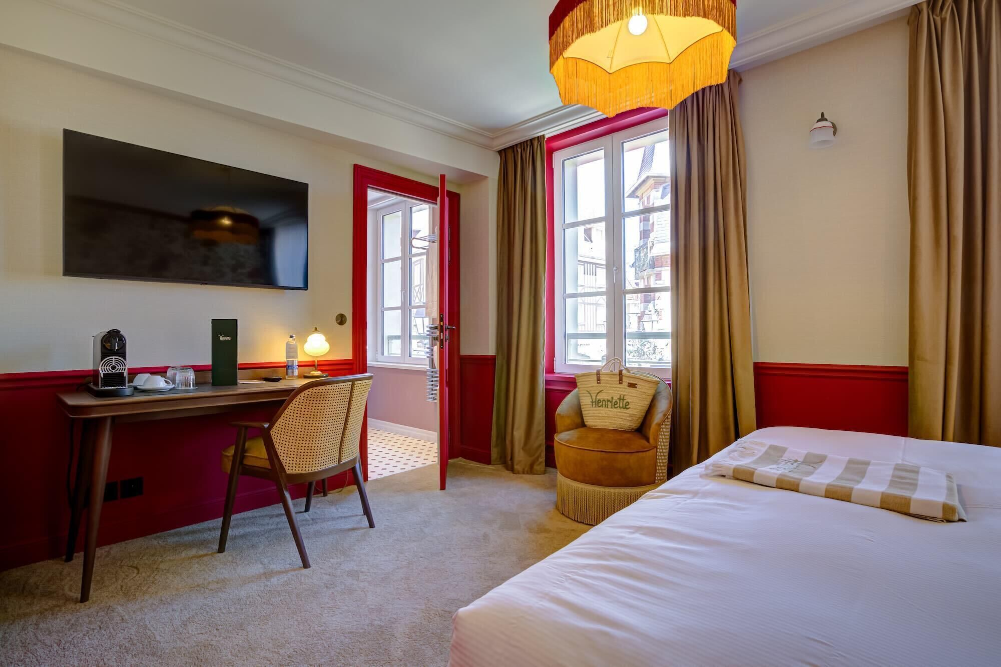 A hotel room with a bed, a desk, a chair, a television, and a window with curtains.
