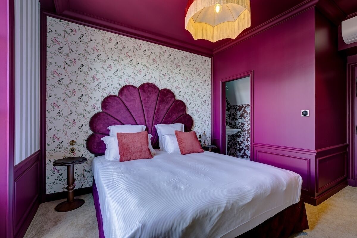A room with a bed, a small table, a decorative headboard, and a hanging light fixture.