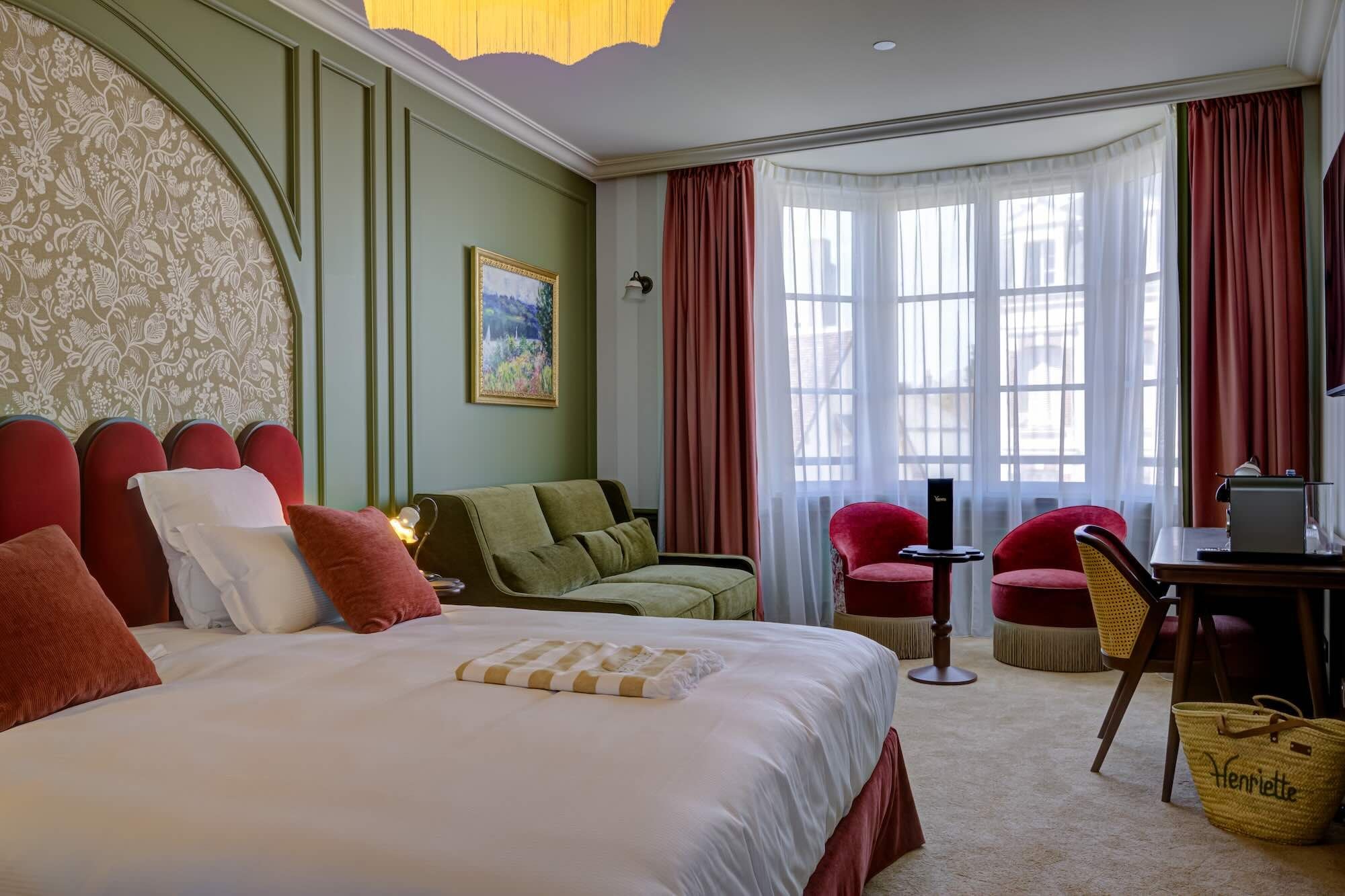 A hotel room with a large bed, a desk, a chair, and a window with curtains.