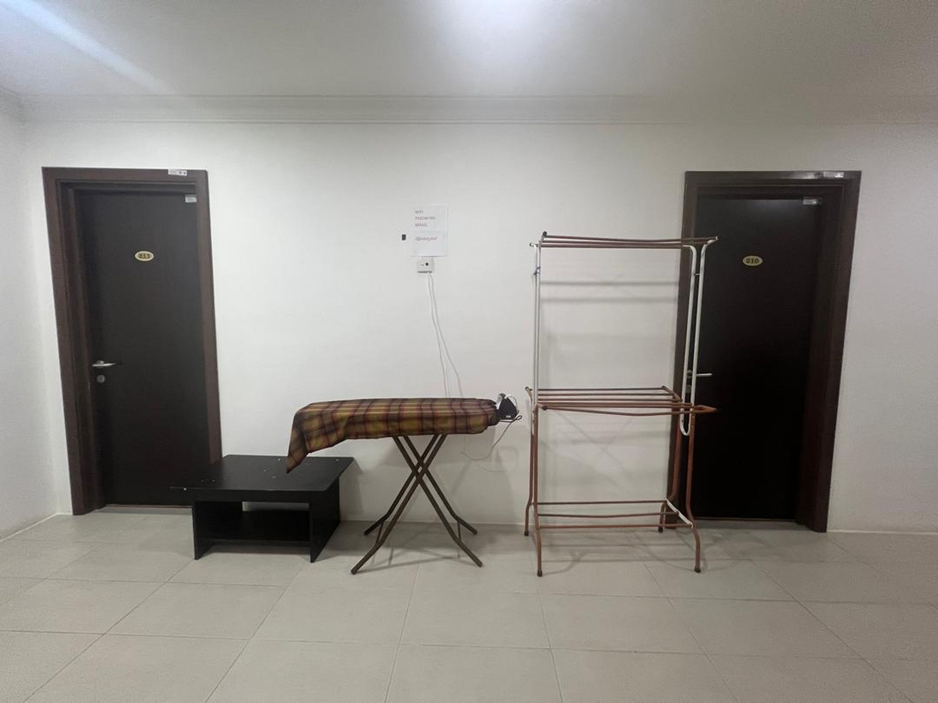 A room with a black ironing board, a metal drying rack, and two dark wooden doors.