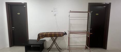 A room with a black ironing board, a metal drying rack, and two dark wooden doors.