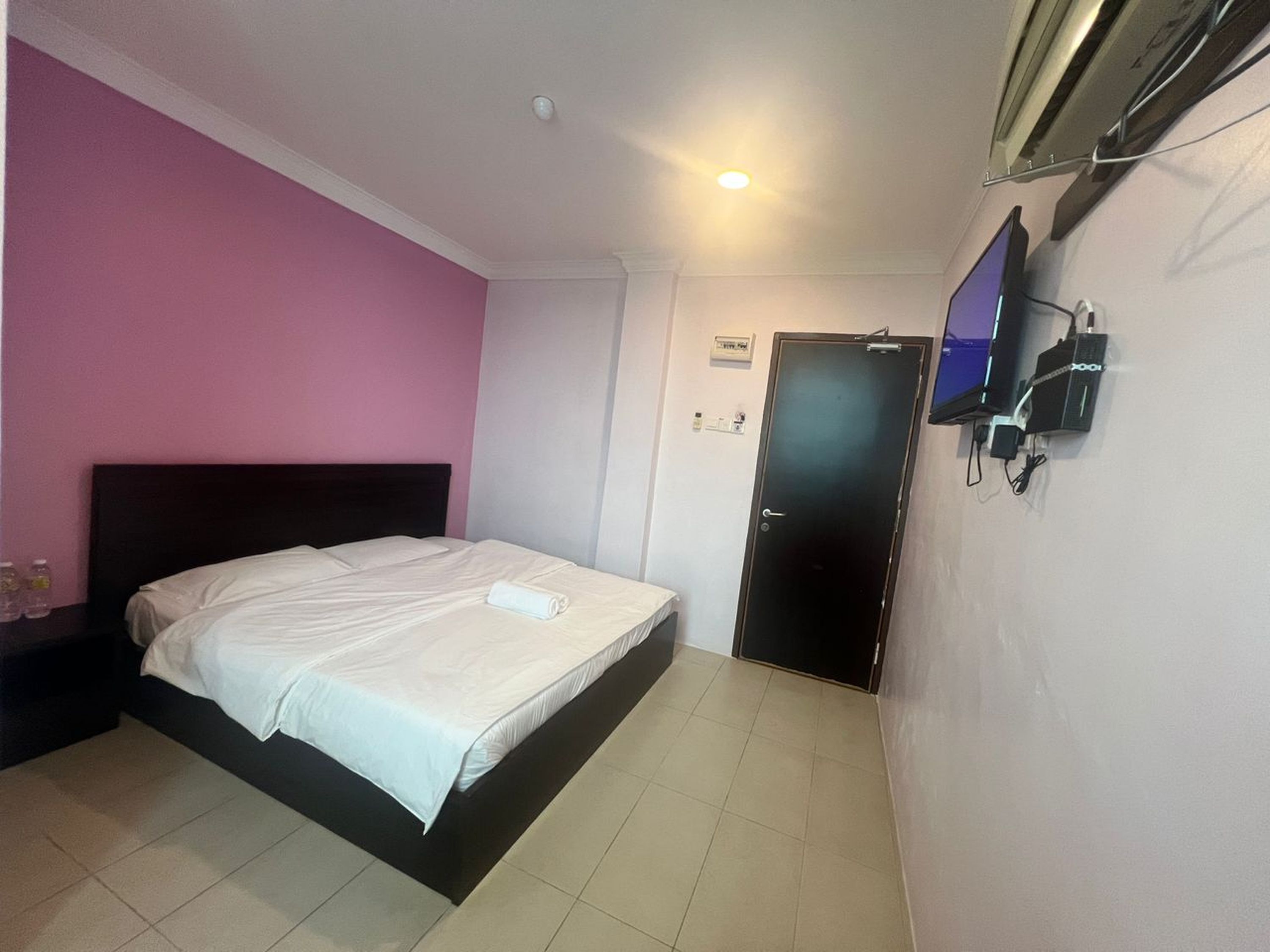 Une chambre d’hôtel avec un lit, un téléviseur fixé au mur et une porte.