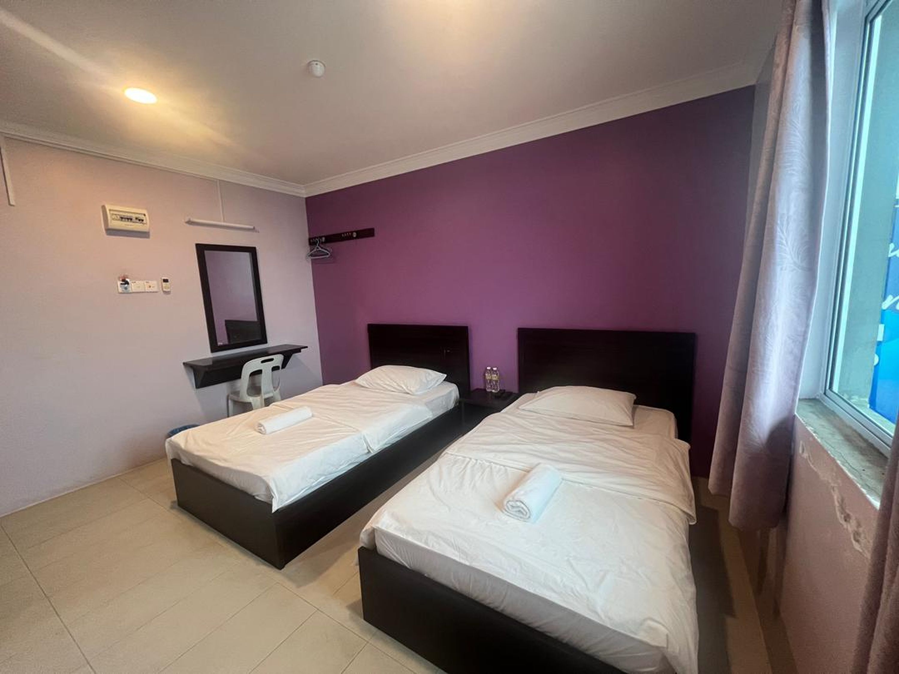Habitación de hotel con dos camas individuales, un escritorio con silla, un espejo y una ventana con cortinas.