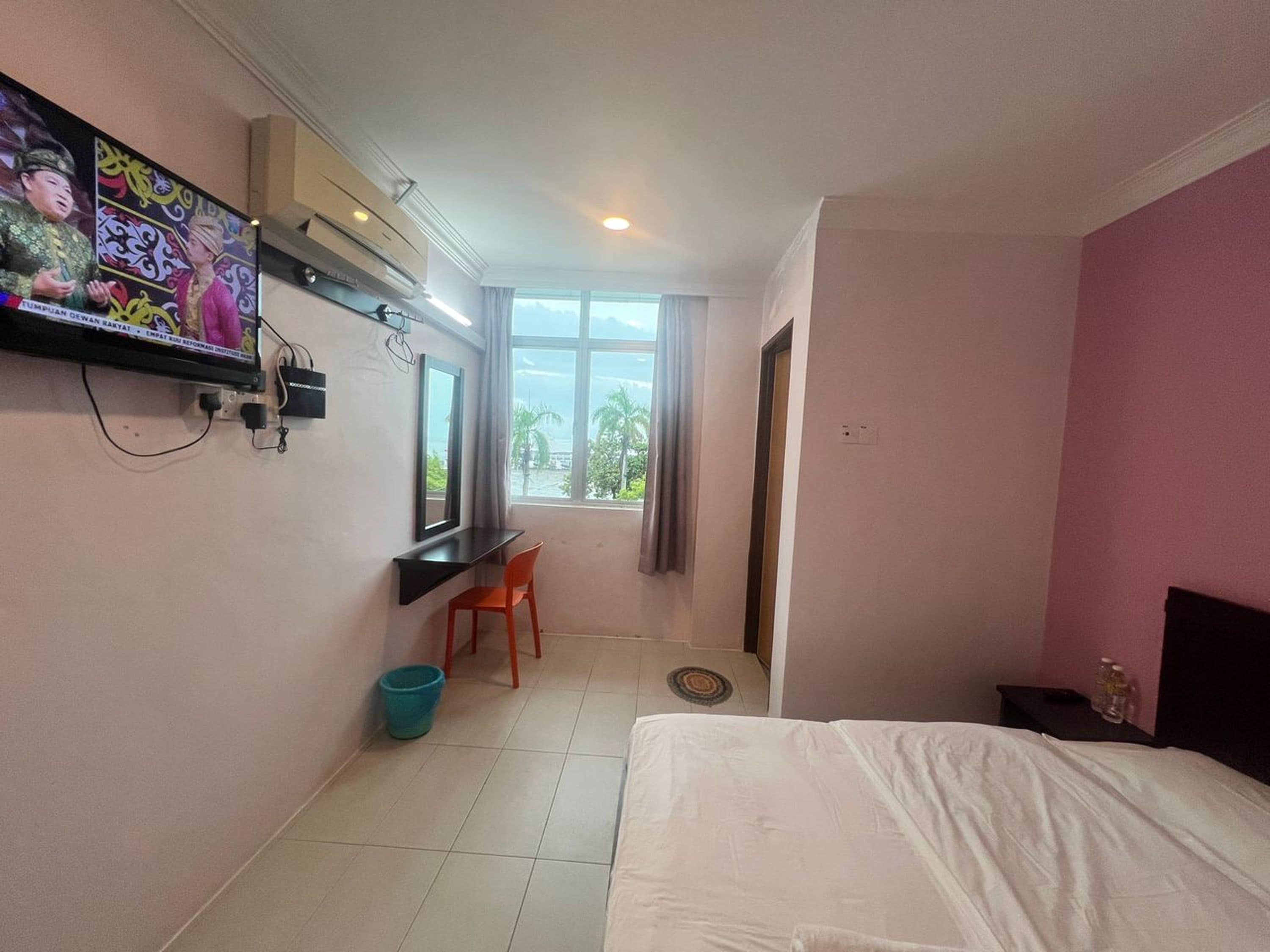 Une chambre d’hôtel avec un lit, un bureau et une chaise, un téléviseur fixé au mur et une fenêtre donnant sur des palmiers.