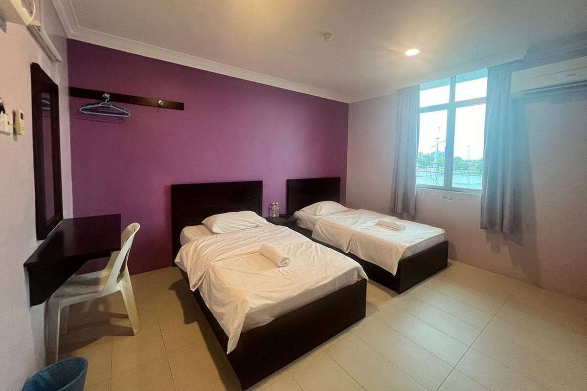 A hotel room with two beds, a desk, a chair, and a window with a view.