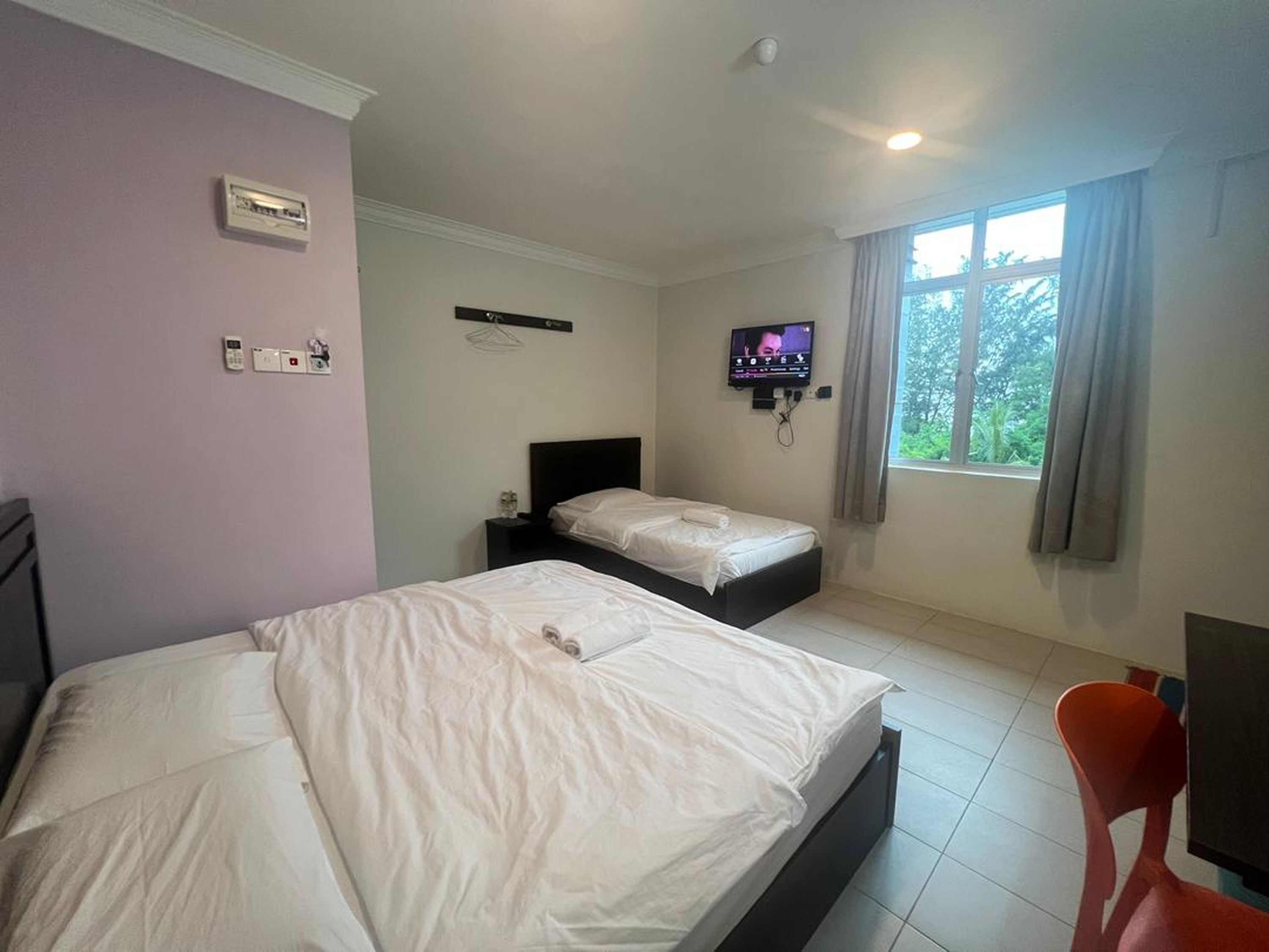 A hotel room with two beds, a TV, a window with curtains, and a red chair.