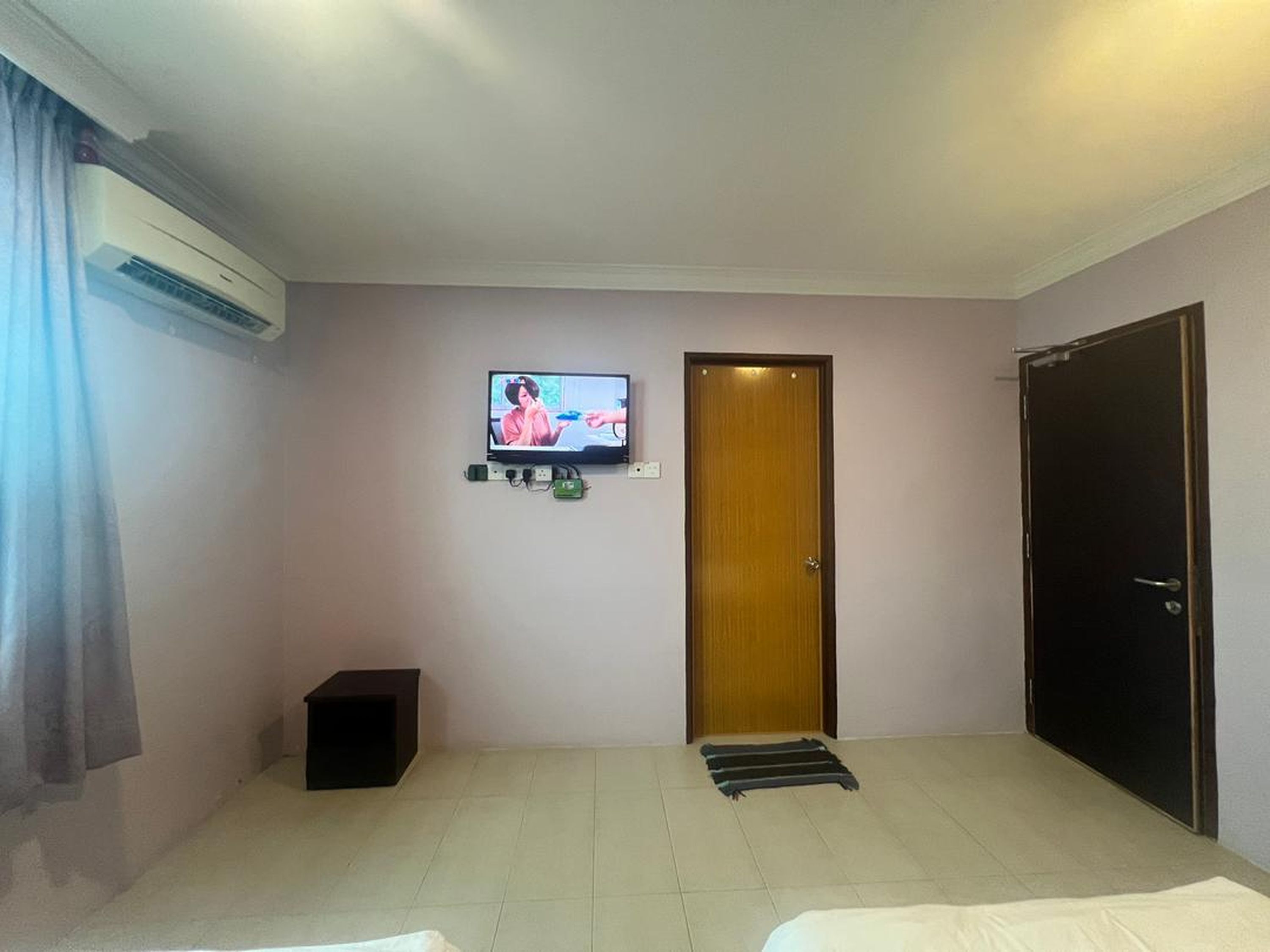 A hotel room with a television mounted on the wall, a wooden door, a black cabinet, and a black wardrobe.