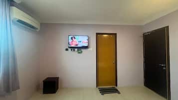 A hotel room with a television mounted on the wall, a wooden door, a black cabinet, and a black wardrobe.