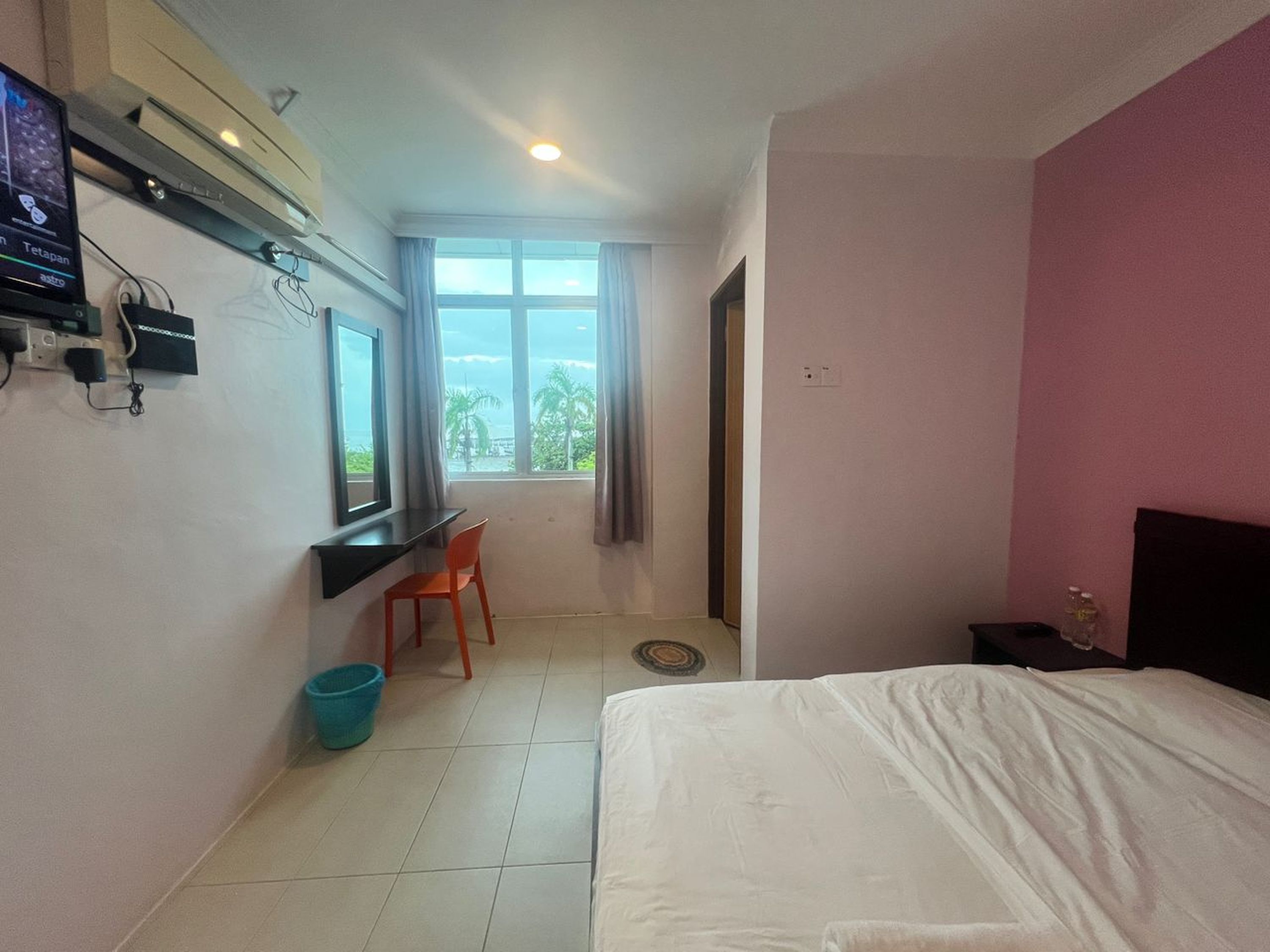 A hotel room with a bed, a desk with a chair, a TV, and a window with curtains.