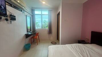 A hotel room with a bed, a desk with a chair, a TV, and a window with curtains.