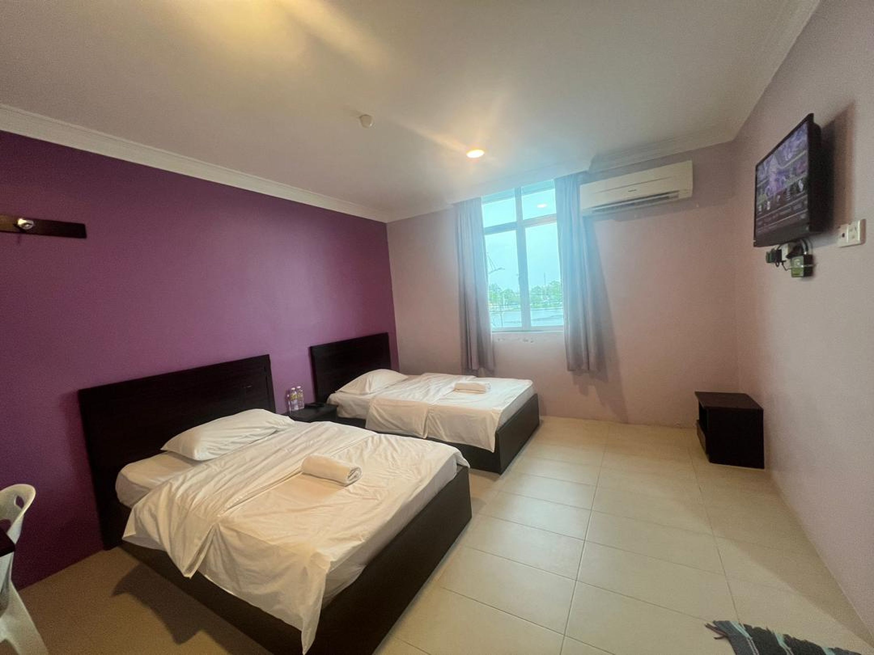 A hotel room with two beds, a TV, and a window with curtains.