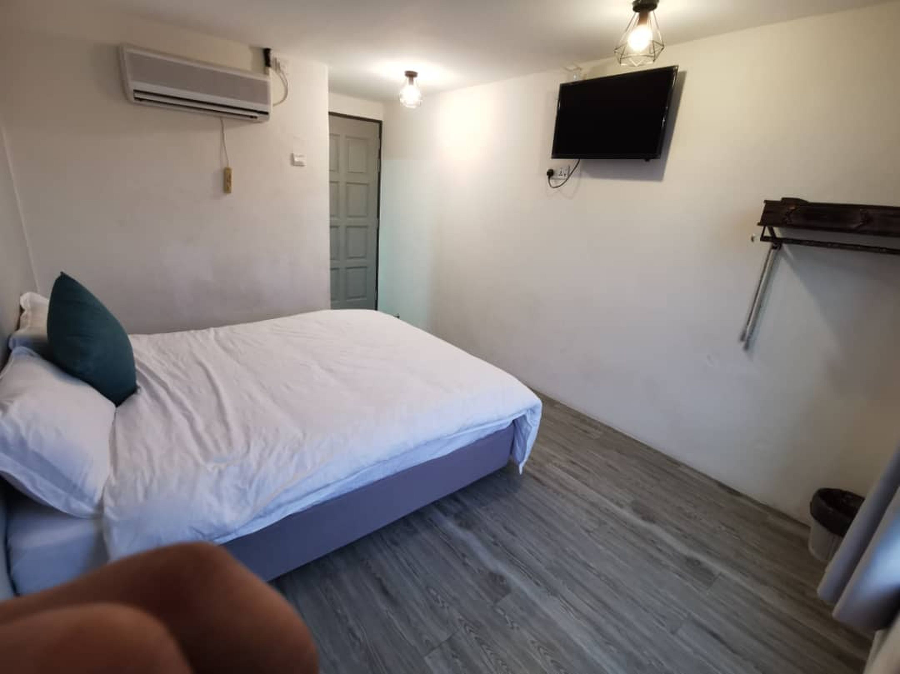 A bedroom with a bed, an air conditioning unit, a mounted TV, and a wooden floor.